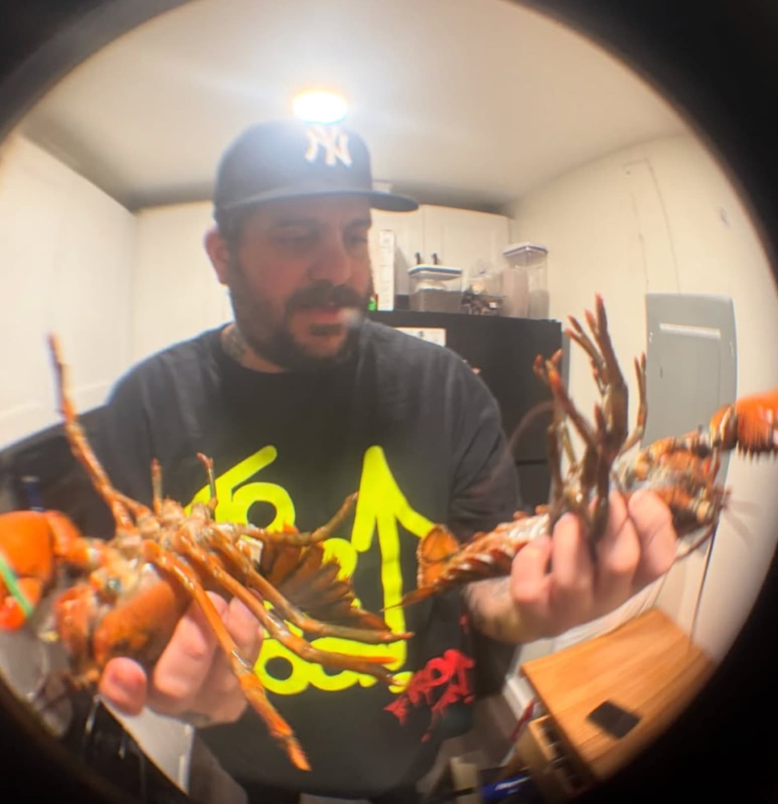 Chef Eduardo Cuenca holding two cooked lobsters in a kitchen, shot with a fisheye lens