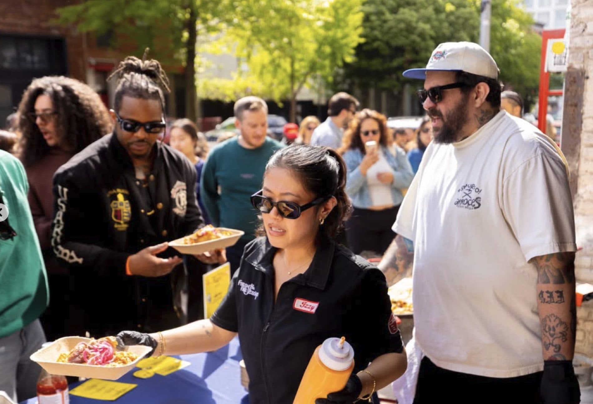 Staff handing a bowl of paella to a guest while Chef Ed stands nearby at an outdoor pop-up