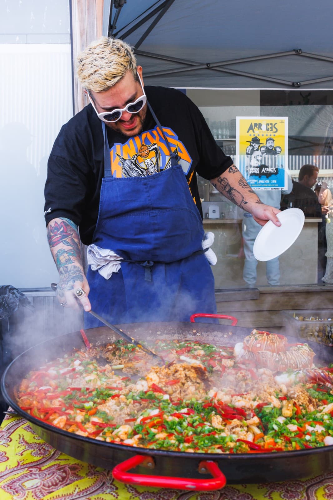 Chef stirring a steaming paella pan topped with seafood, peppers, and scallions