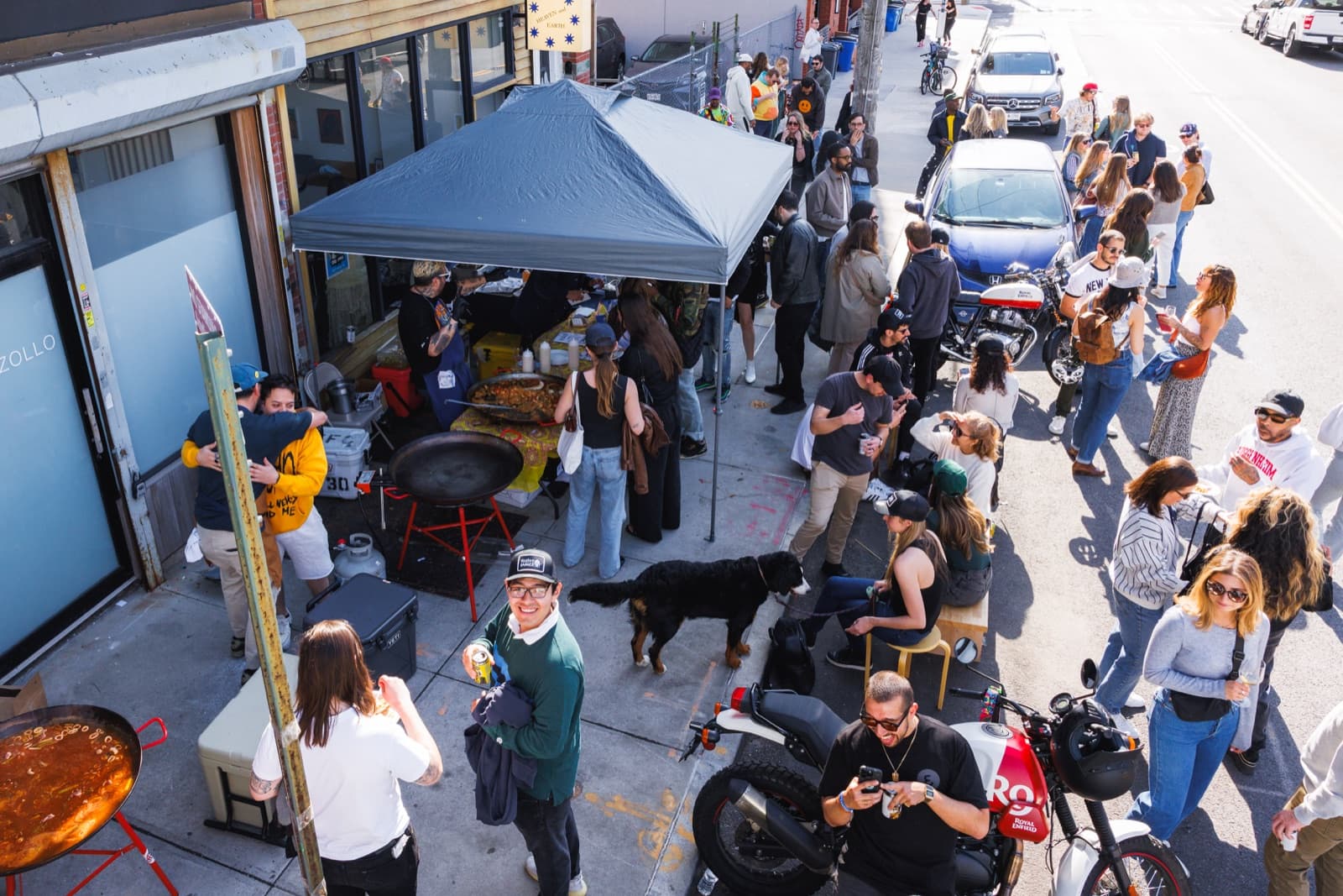 High-angle view of a crowded sidewalk paella party with pans, tents, and guests
