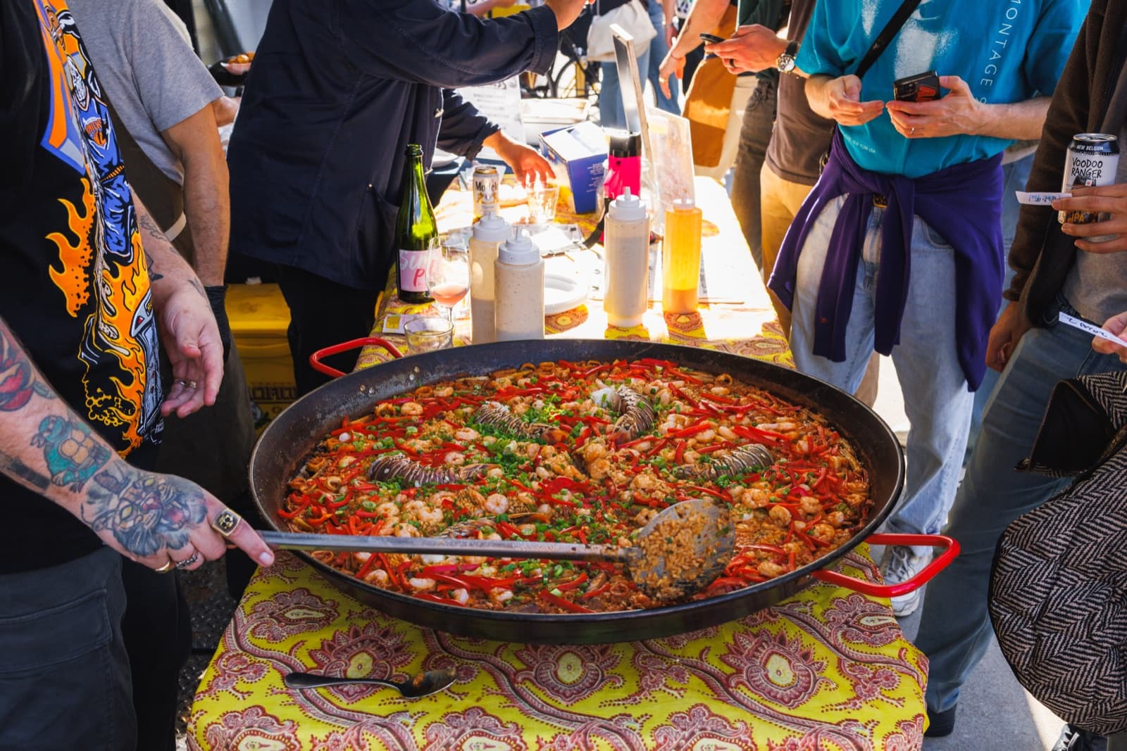 Large seafood paella with lobster and shrimp on a patterned tablecloth surrounded by guests